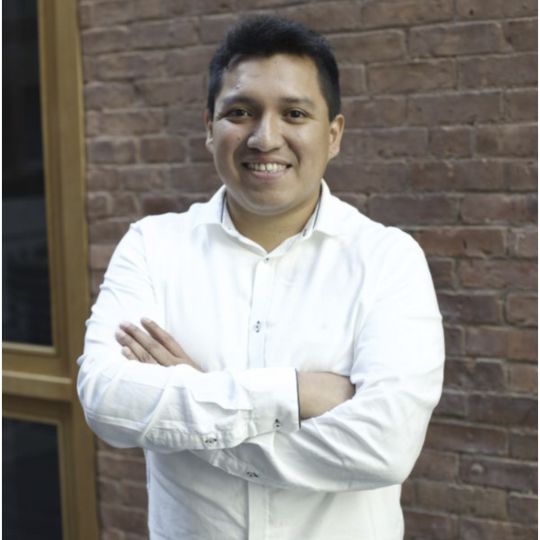 A smiling man in a white shirt in front of a brick wall