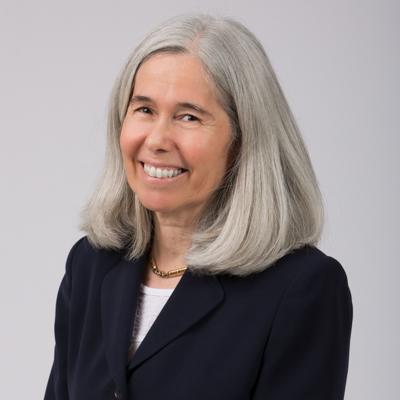 Photo of Sarah Lamitie. She is a white woman with shoulder length gray hair wearing a black blazer. She is smiling at the camera.