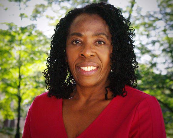 Maria Latimore faces the camera. She is wearing a red shirt and standing in front of trees.