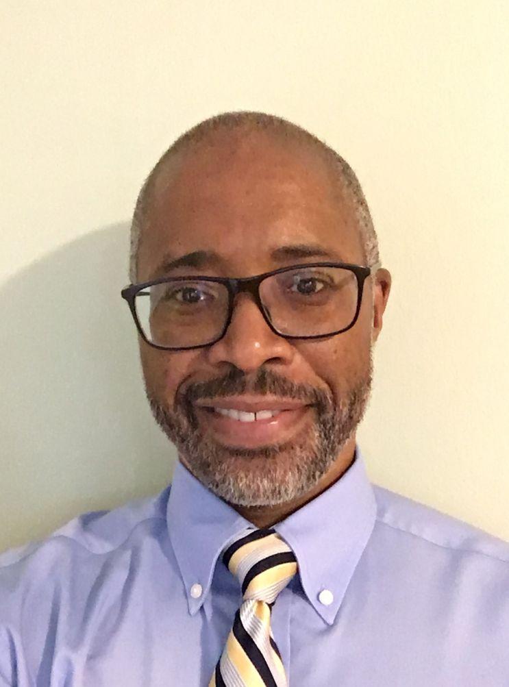 A portrait of a smiling man in front of a cream wall