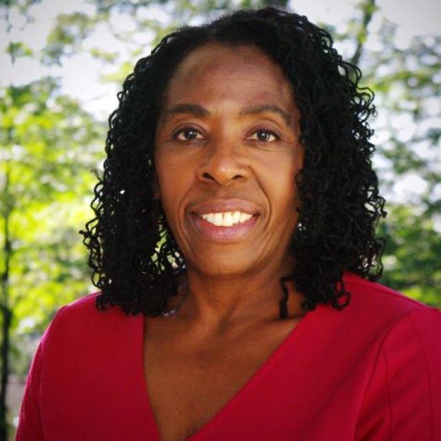 Maria Latimore faces the camera. She is wearing a red shirt and standing in front of trees.