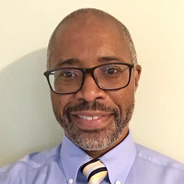 A portrait of a smiling man in front of a cream wall